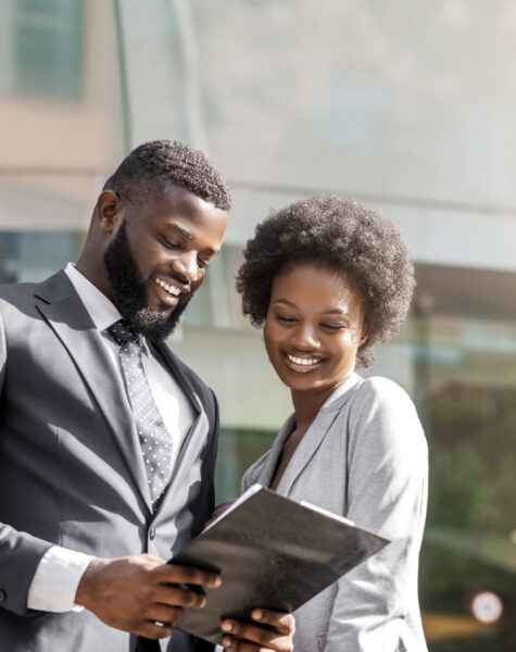 Couple of African business partners reading finance reports outdoors, happy about monthly results of their company. Panorama with free space